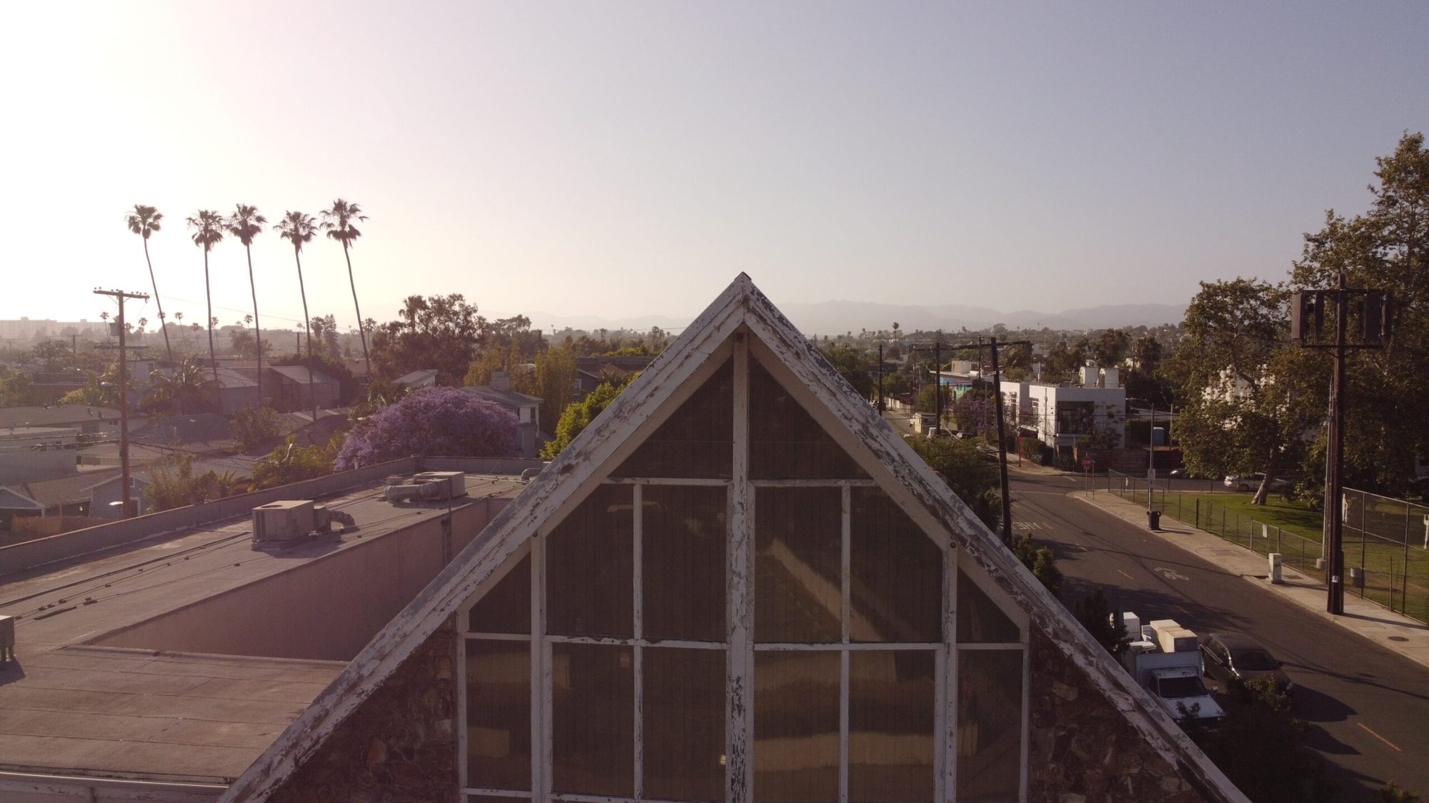 Aerial view of a church gable over Oakwood at golden hour, with palm trees and hills behind