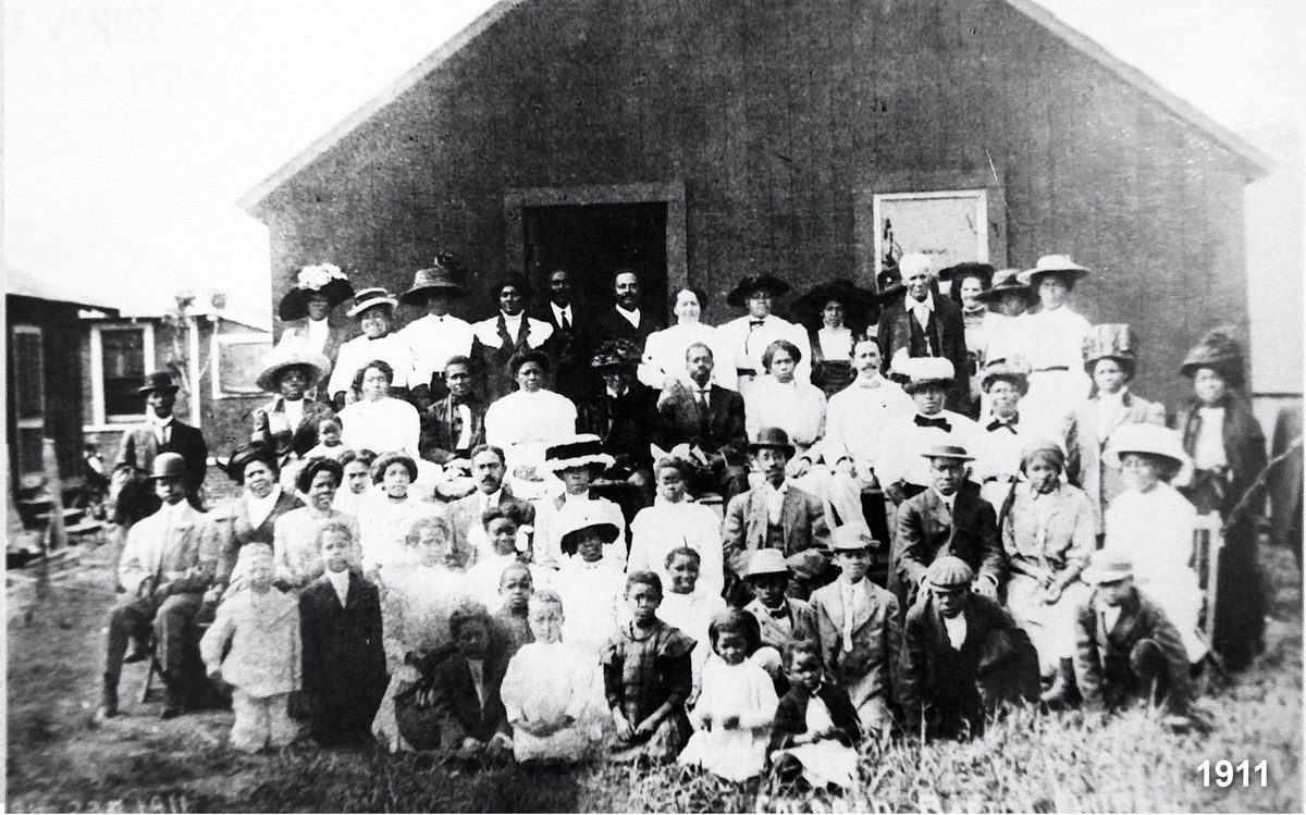 Black and white group photo of a Venice community gathered in front of a wooden building in 1911